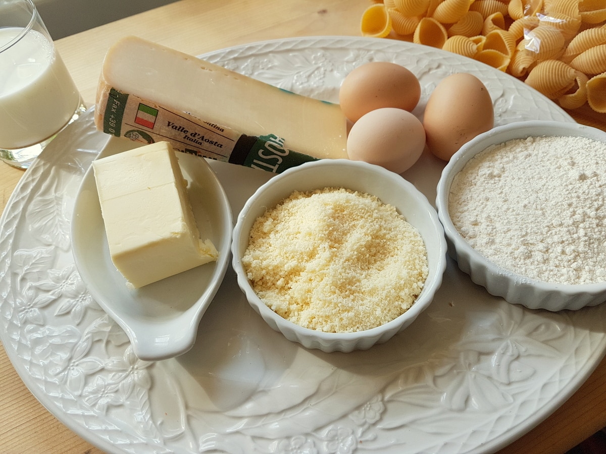 Ingredients for conchiglie al forno (baked pasta shells) on white plate.