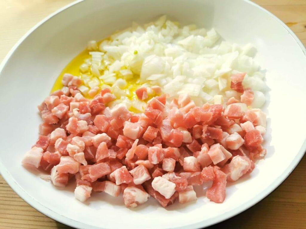 pancetta cubes and chopped onion in pan with olive oil