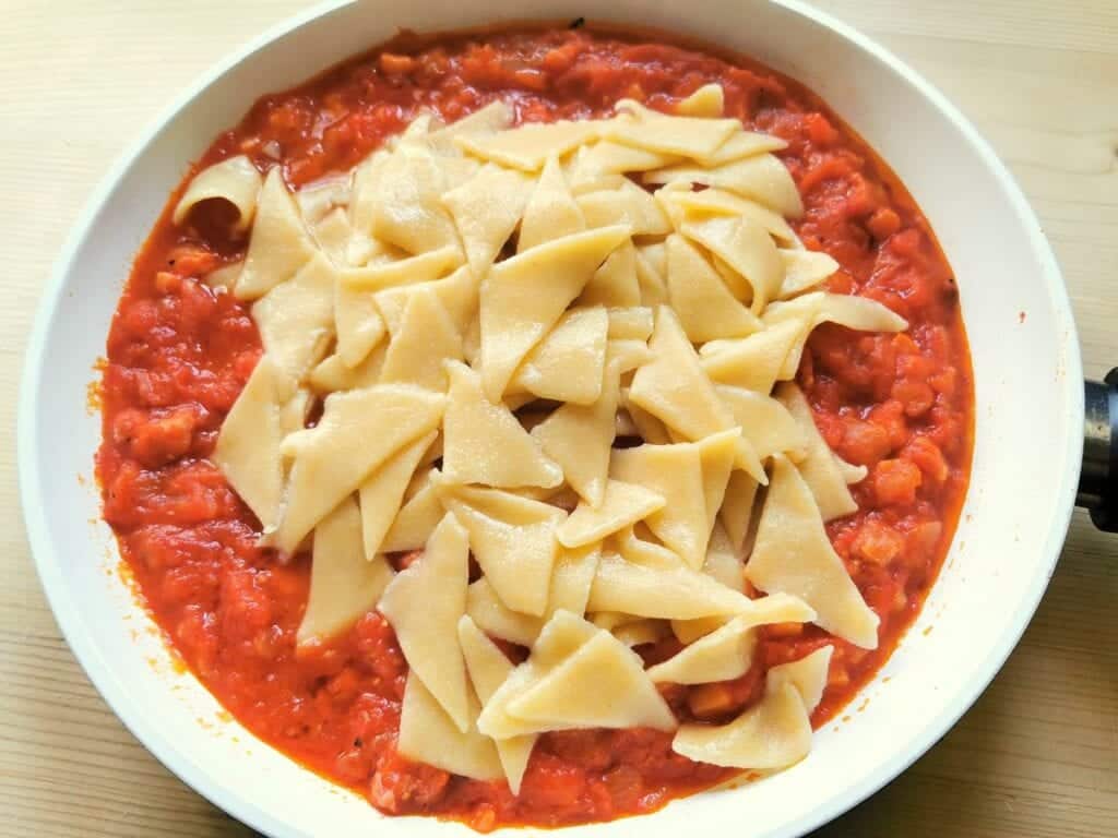 cooked corn and wheat flour pasta triangles in pan with sauce
