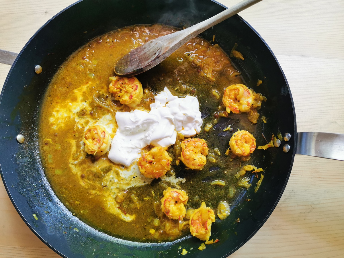 Heavy cream added to skillet with prawns and saffron sauce.
