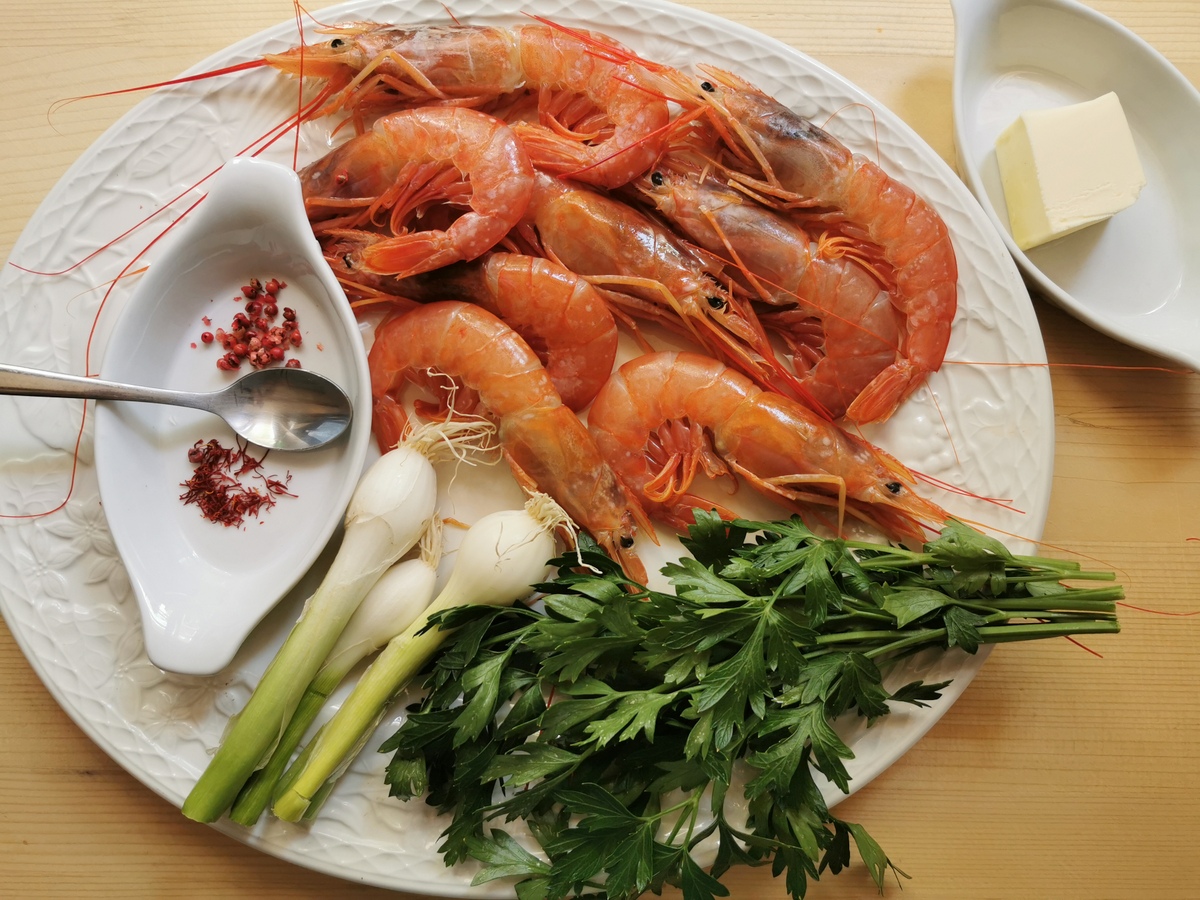 Large shrimp, spring onions, fresh parsley, saffron threads, and pink pepper corns on white plate.