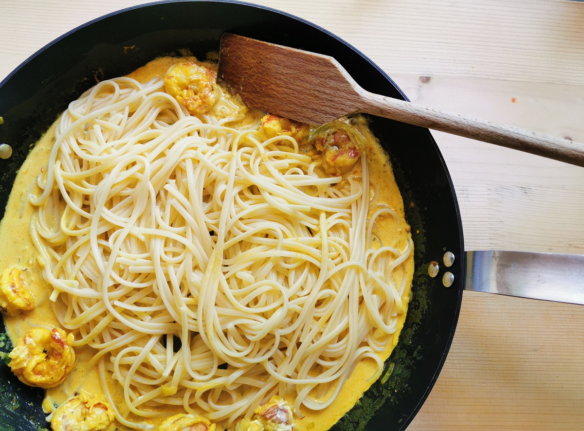 Cooked linguine added to prawn saffron sauce in skillet.