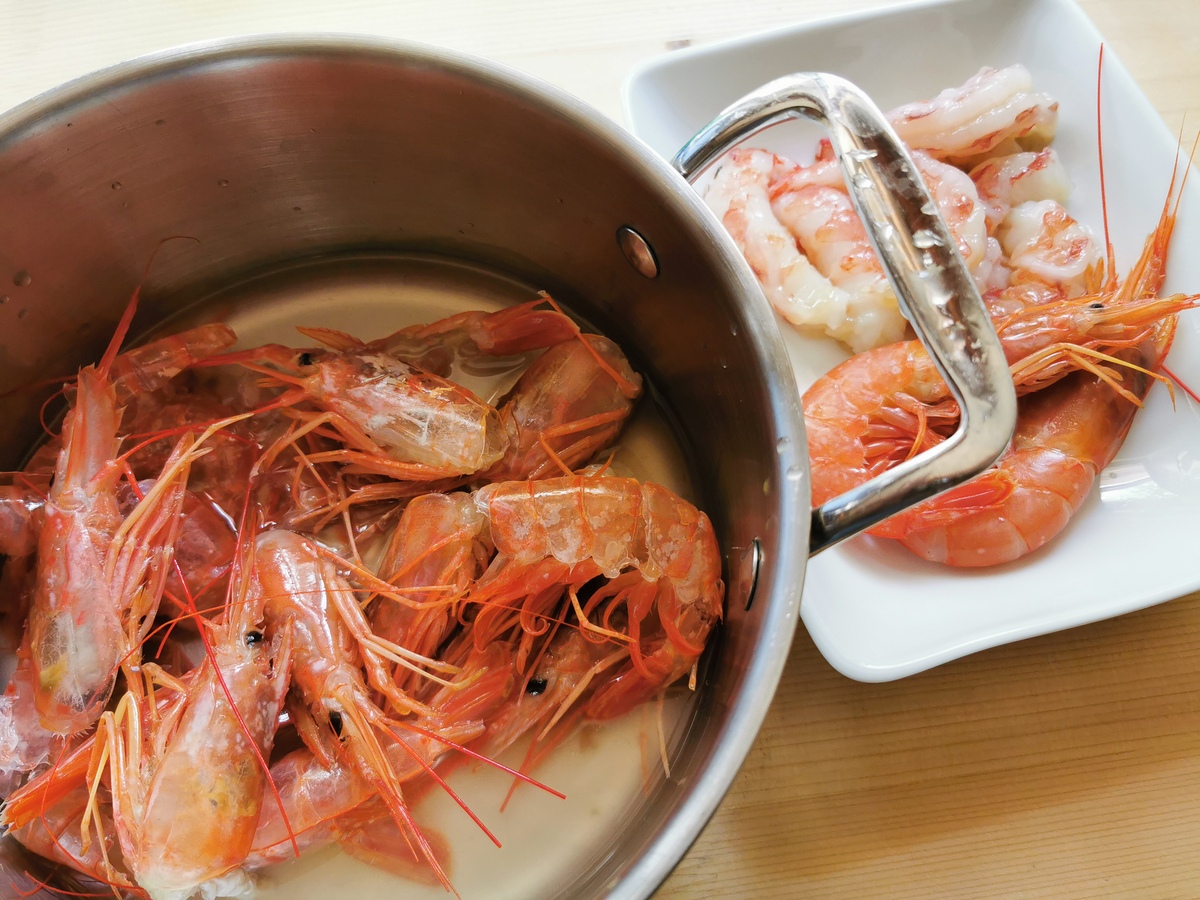 Prawn heads and shells in saucepan and peeled prawns in white bowl.
