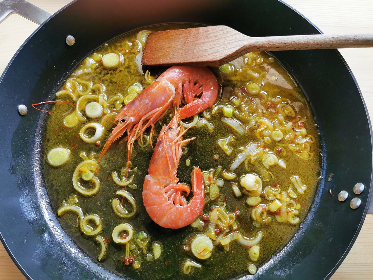 Large unpeeled prawns (shrimp) in skillet with cooked spring onions and saffron prawn broth.