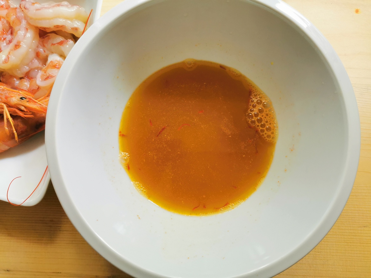 Saffron soaking water mixed with prawn broth in white bowl.