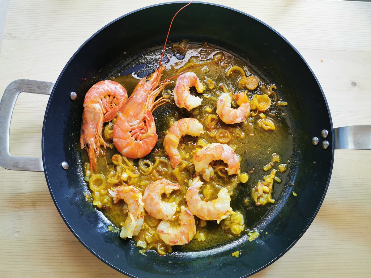 Peeled prawns added to skillet with unpeeled prawns, spring onion and saffron sauce.