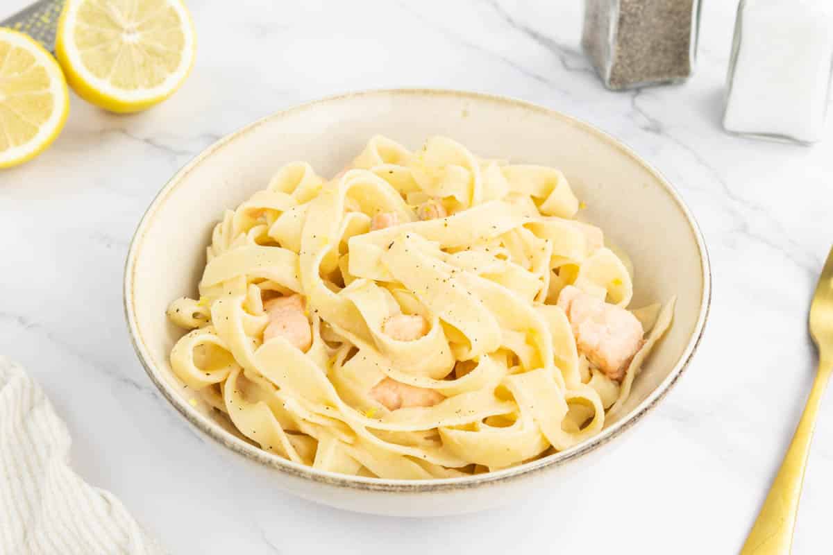 Creamy lemon salmon pasta in a bowl with two half lemons in the background.