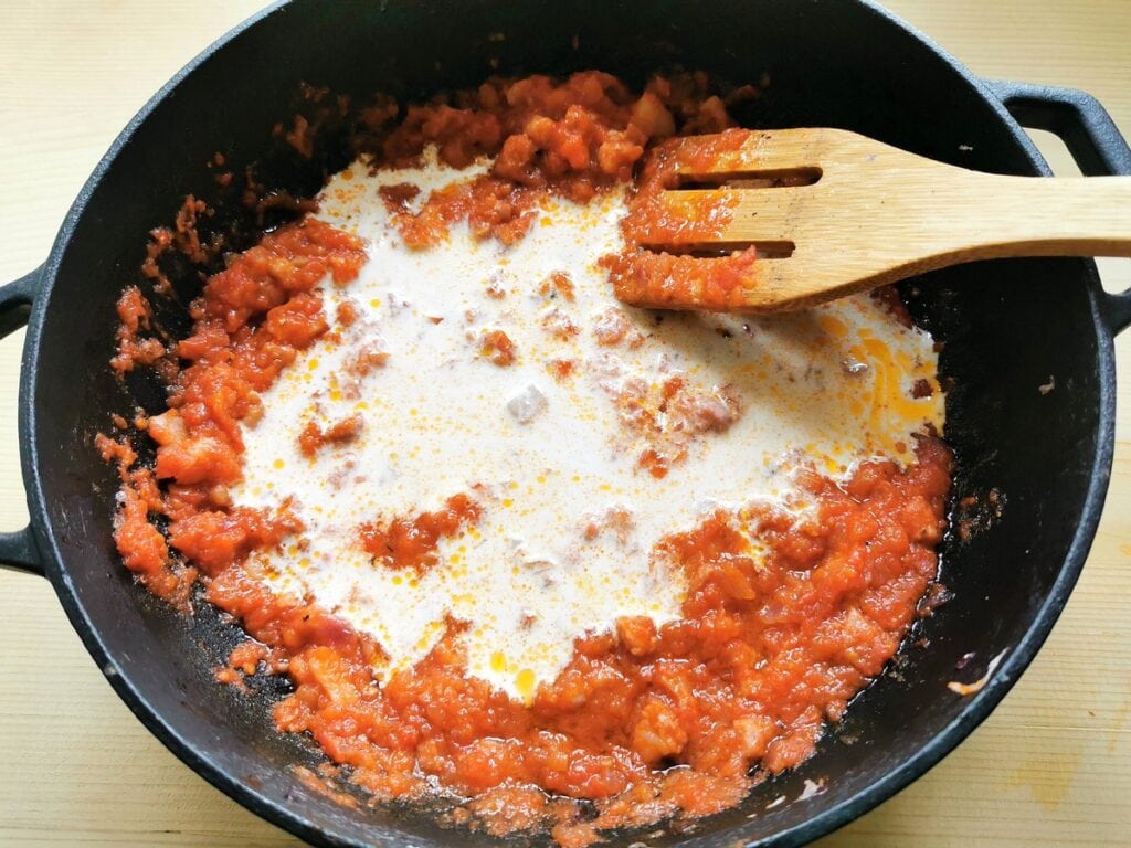 Fresh cream added to tomato and pancetta sauce in skillet