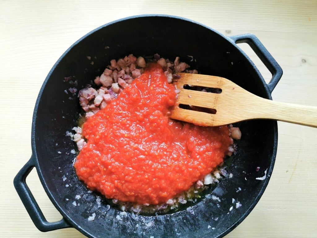 tomato passata added to onion and pancetta in skillet