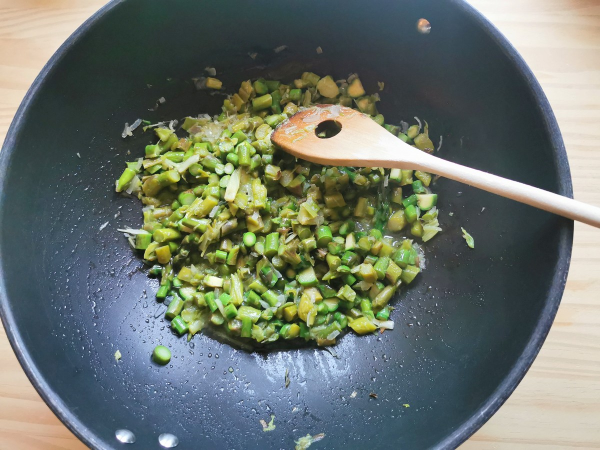 Peeled and chopped white onion and cut asparagus stalks cooking in large skillet.