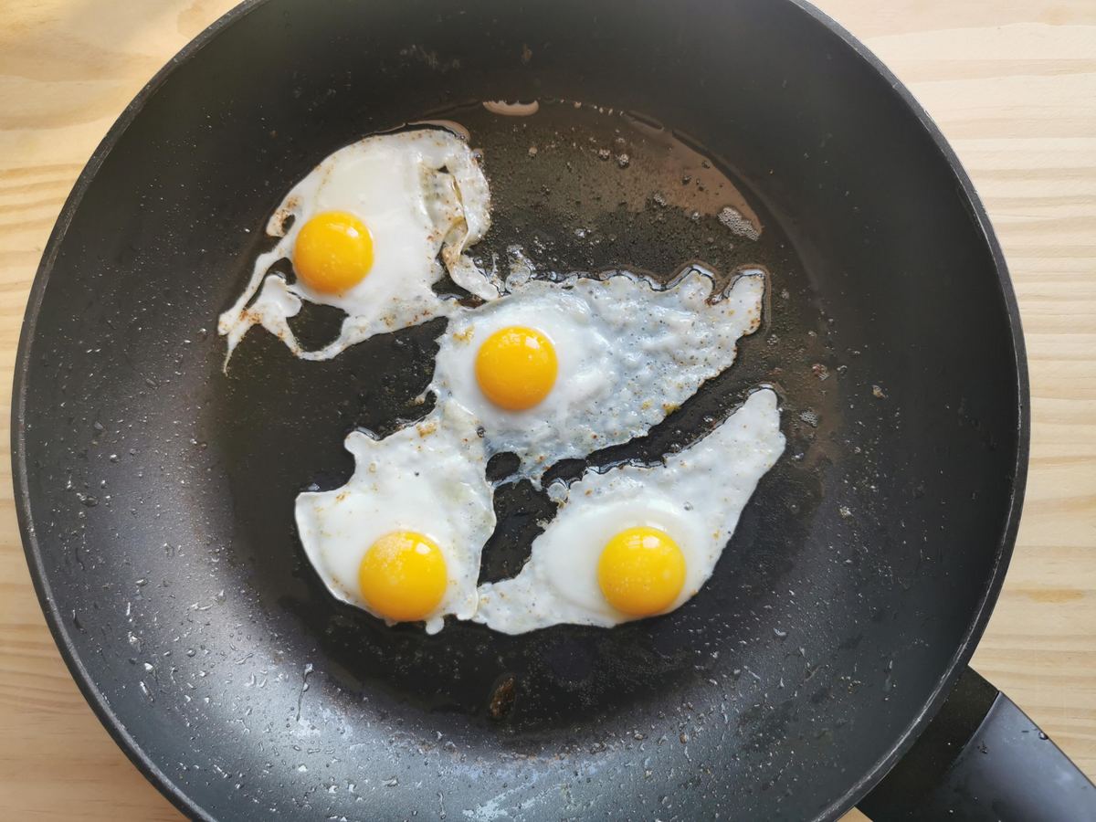 4 quail eggs frying with butter in frying pan.