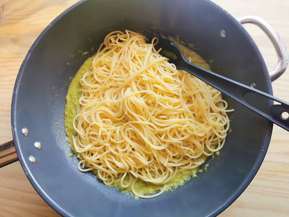 Cooked spaghetti in skillet on top of creamy asparagus sauce.