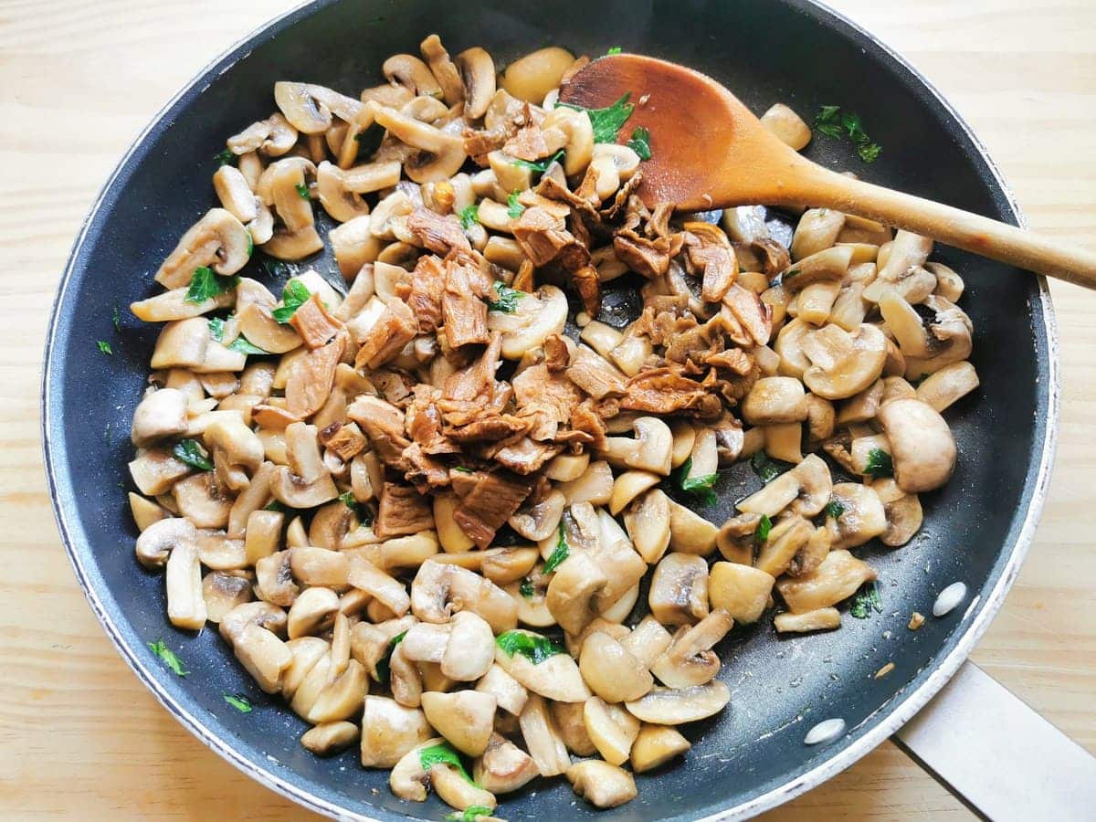 Chopped porcini in skillet with softened button mushrooms and parsley.