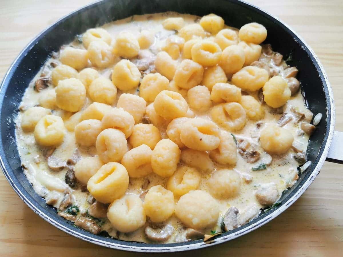 Cooked gnocchi added to mushroom and starcchino sauce in skillet.