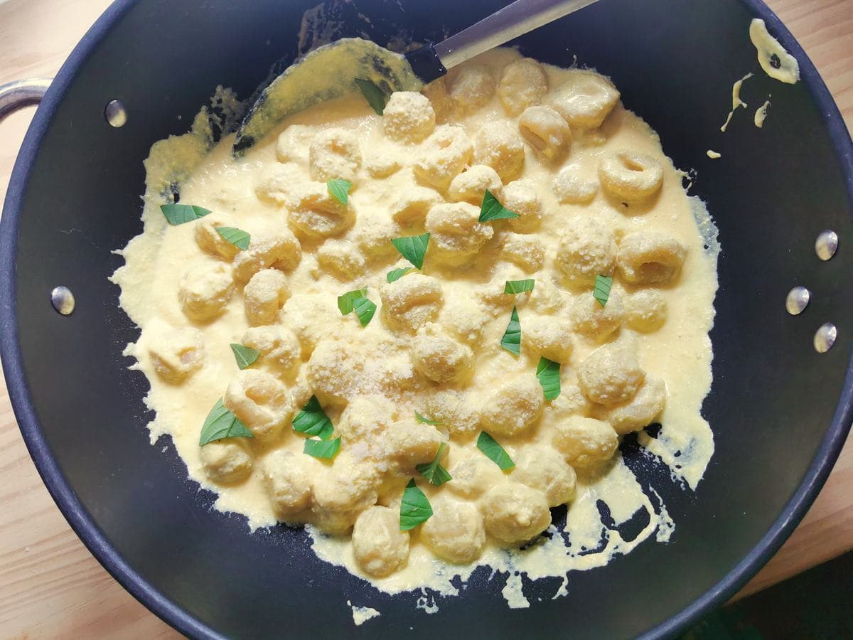 Potato gnocchi mixed with creamy saffron sauce in large pan.