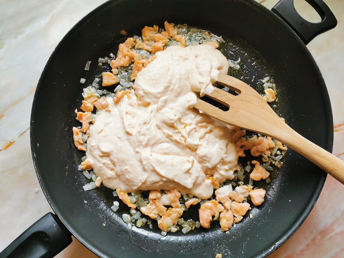 Smoked salmon and cream sauce added to skillet with salmon and onion pieces.