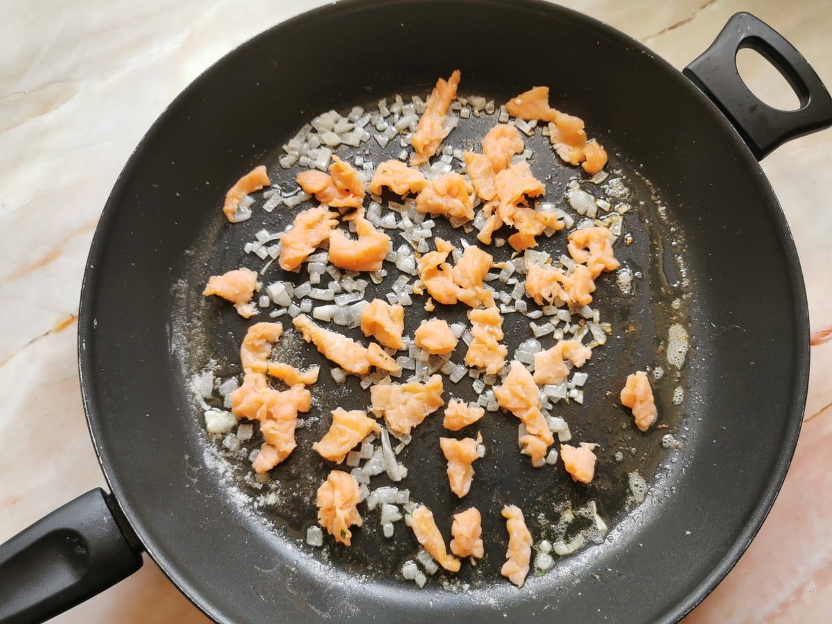 Pieces of smoked salmon and onions with melted butter in skillet.