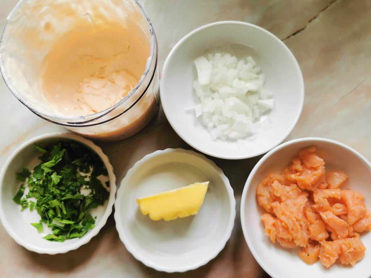 Chopped parsley, peeled and chopped onions, pieces of smoked salmon, salmon cream sauce and a pat of butter in bowls.