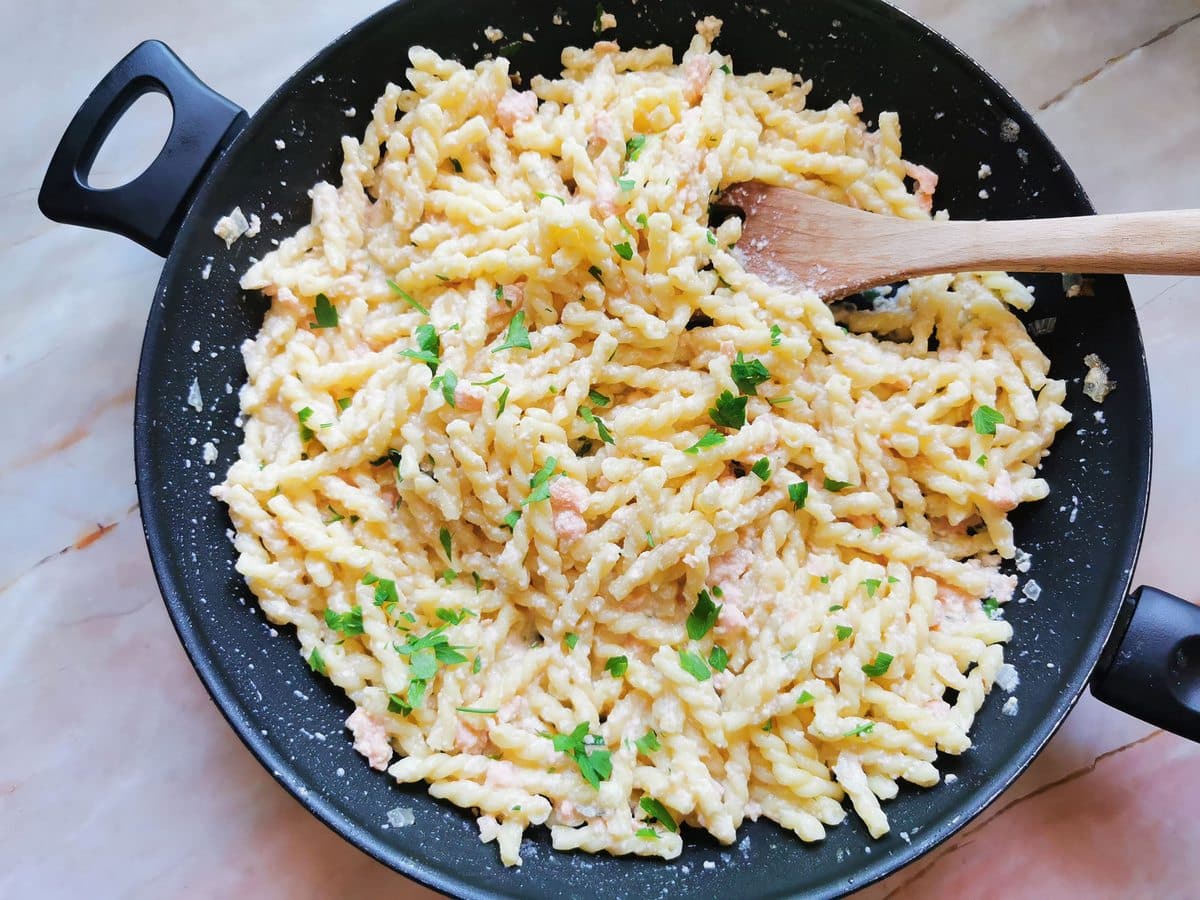 Cooked treccine pasta in skillet with smoked salmon sauce.