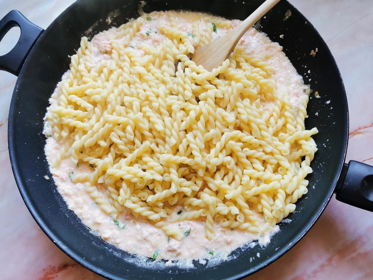 Cooked treccine pasta in skillet with smoked salmon sauce.