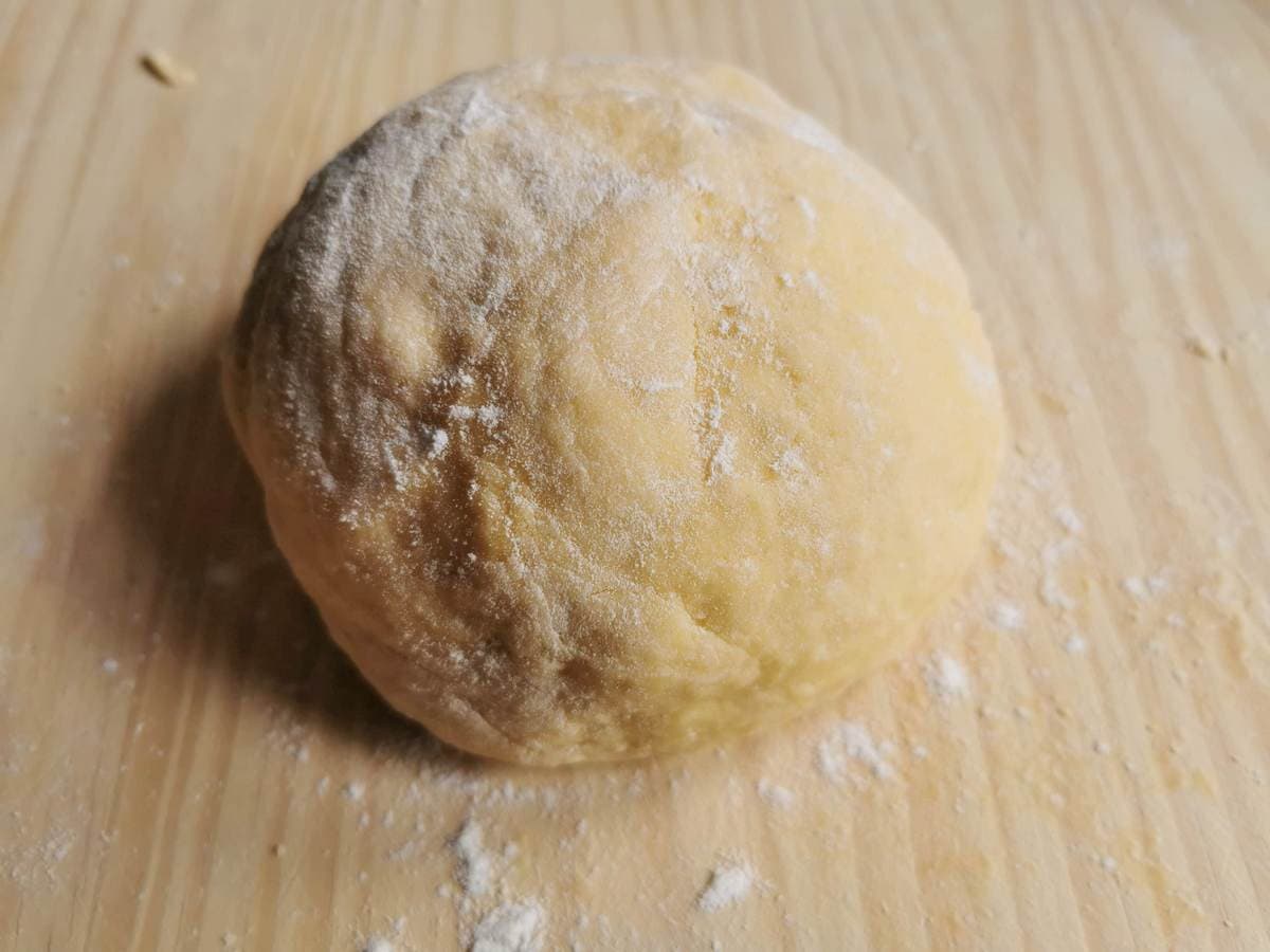 Ball of homemade egg pasta dough on floured wood work surface.