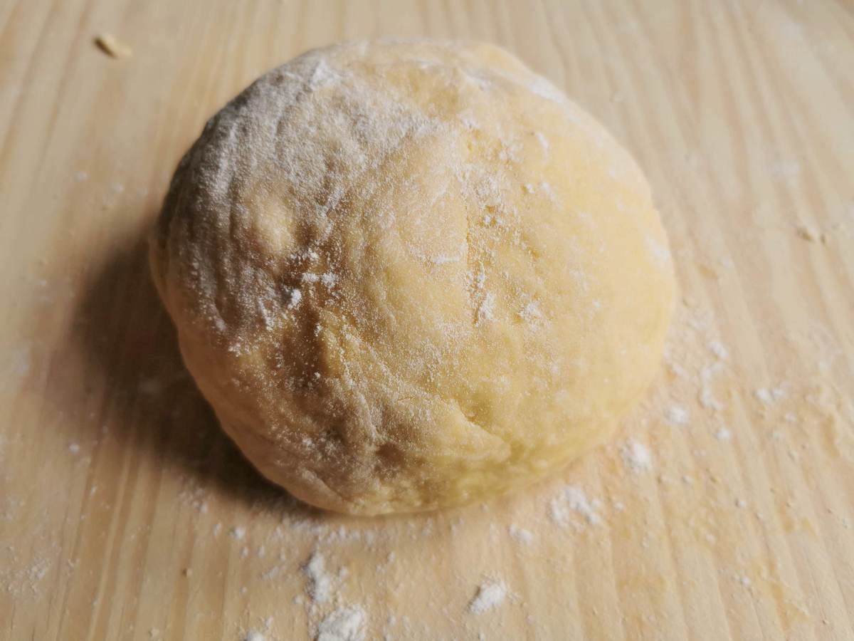 Ball of fresh pasta dough on floured wood work surface.