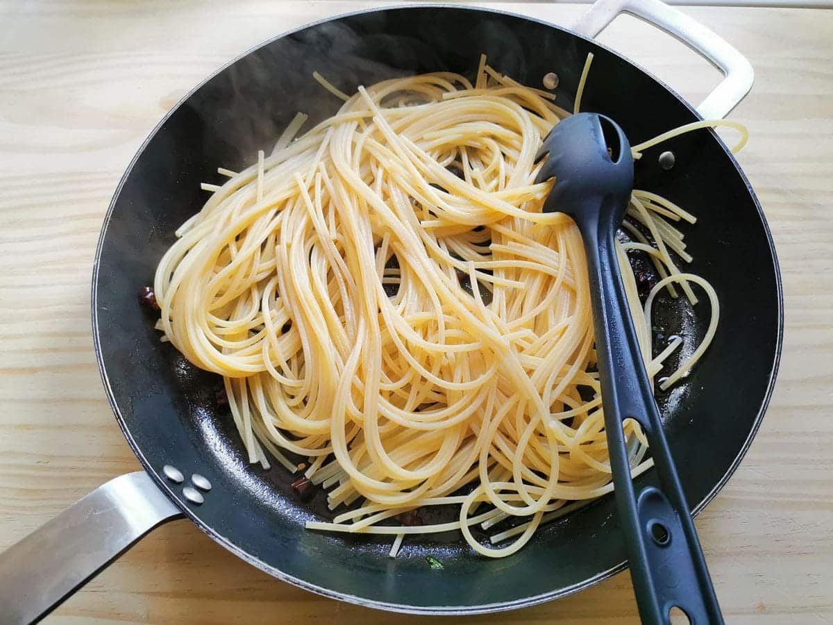 half cooked spaghetti in skillet with garlic, peperoncino and parsley.