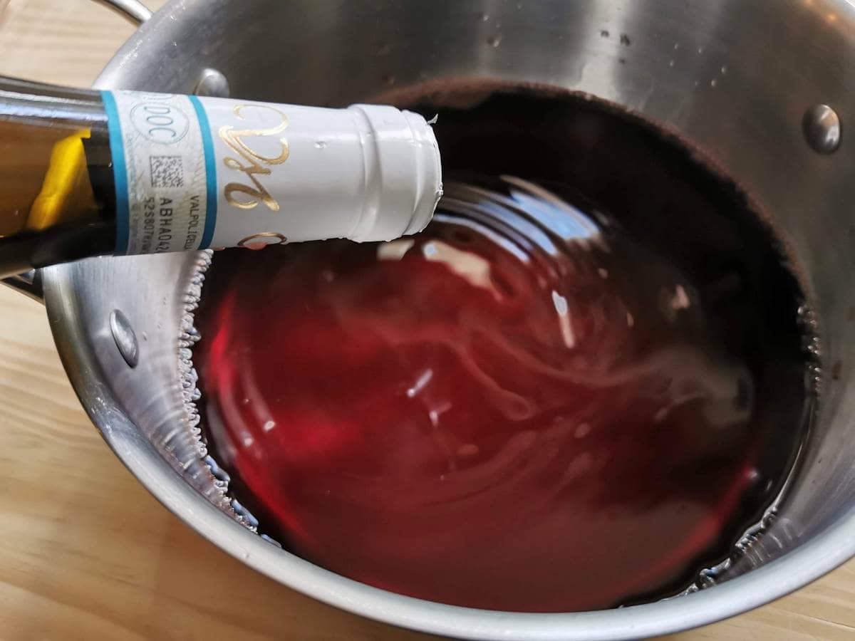 Someone pouring red wine from bottle into saucepan.