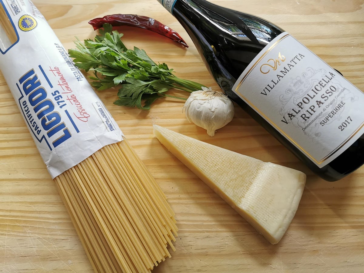 ingredients for red wine pasta on wood surface spaghetti, garlic, parsley, peperoncino, red wine and pecorino.