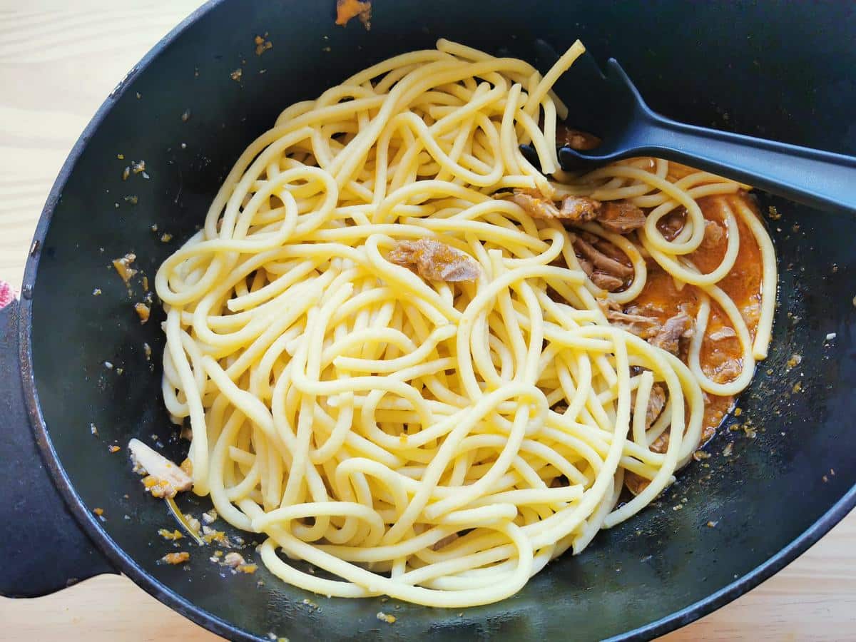 Pasta added to the duck ragu in a pot.