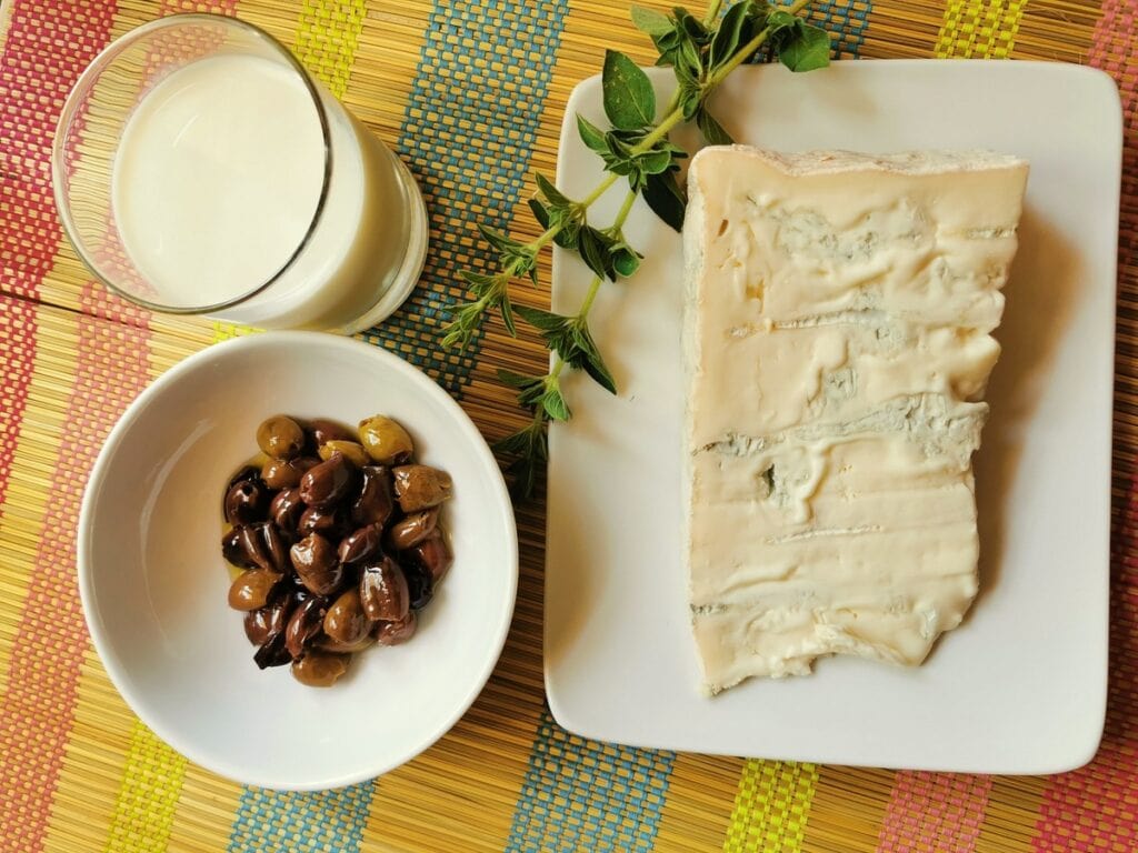 A piece of gorgonzola, some taggiasca olives, a glass of milk and sprigs of marjoram