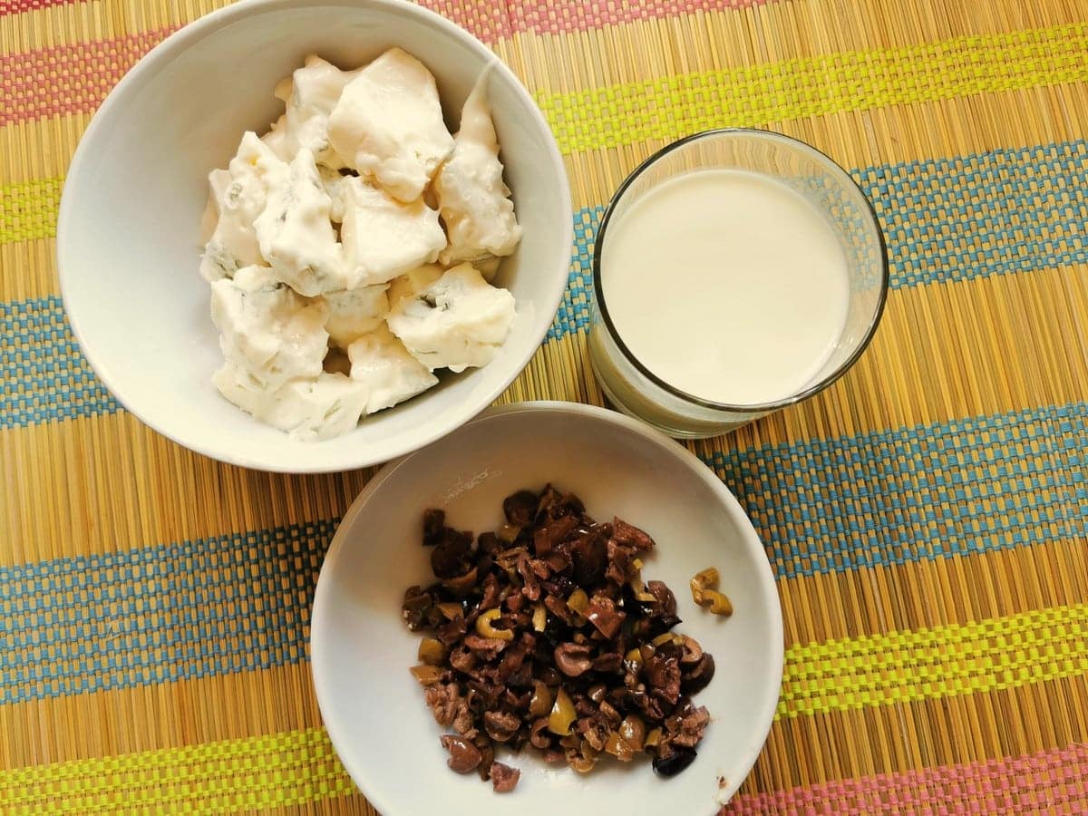 a bowl of chopped taggiasca olive, a bowl of gorgonzola pieces and a glass of milk