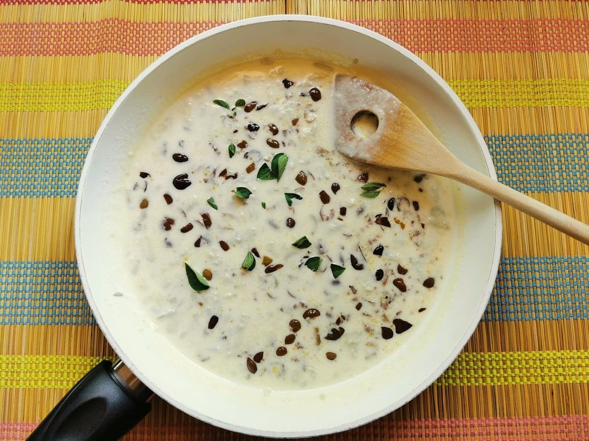 fresh marjoram added to gorgonzola and olives sauce in white pan