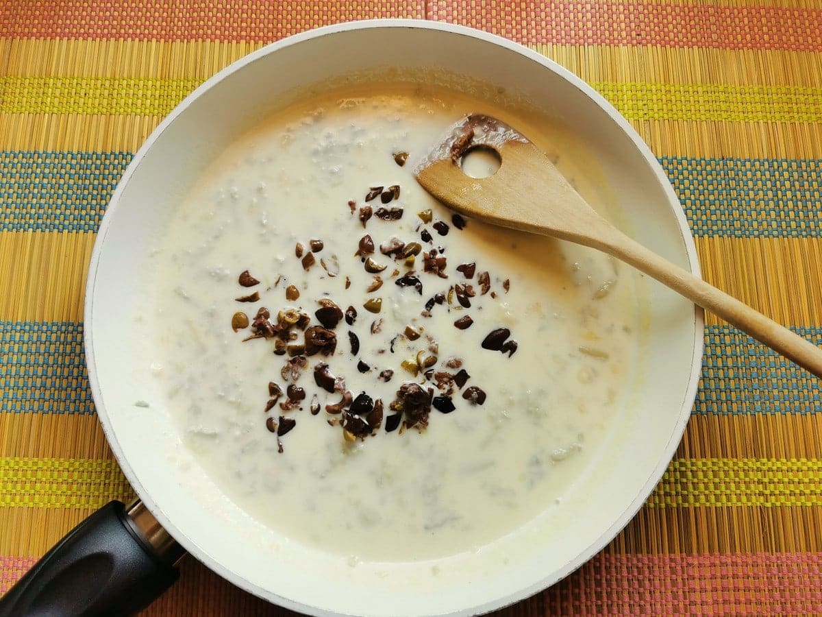 chopped taggiasca olives added to Gorgonzola sauce in white pan