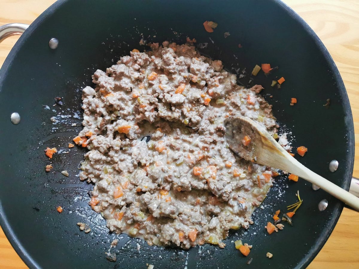 Beef ragu and béchamel and Parmigiano mixed together in skillet.