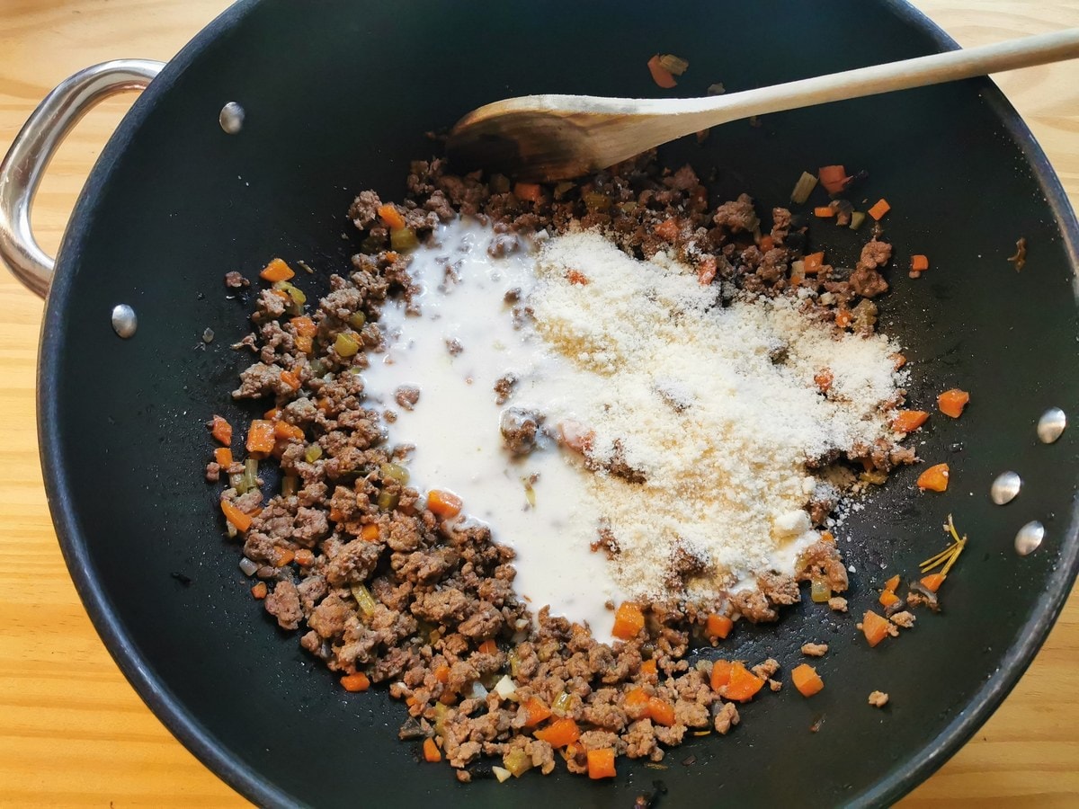 Béchamel sauce and grated Parmigiano added to beef ragu in skillet.