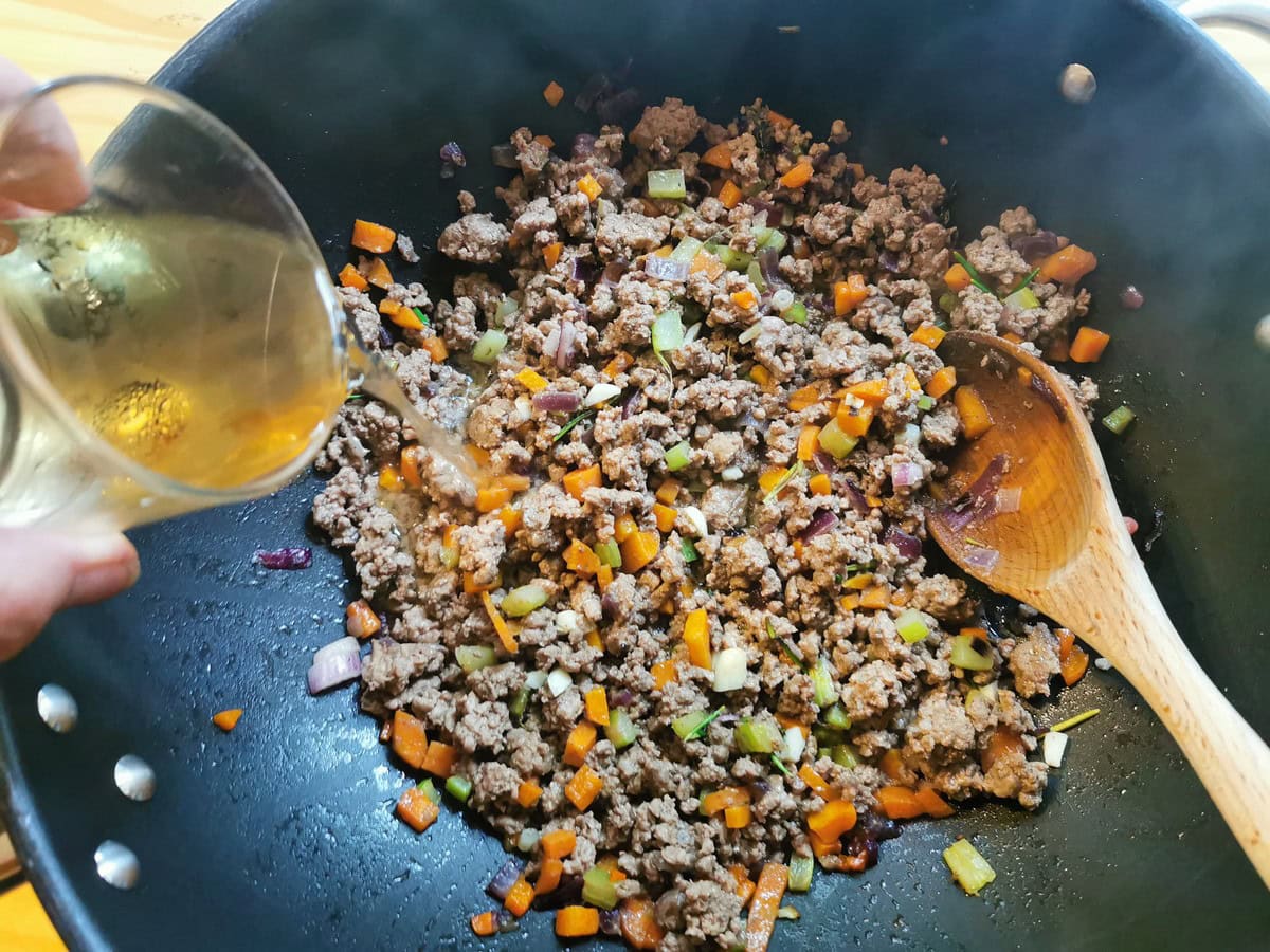 White wine being poured into beef ragu in skillet.