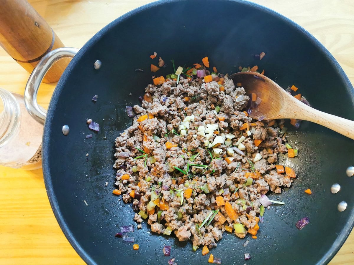 Chopped garlic and herbs added to skillet with browned ground beef.