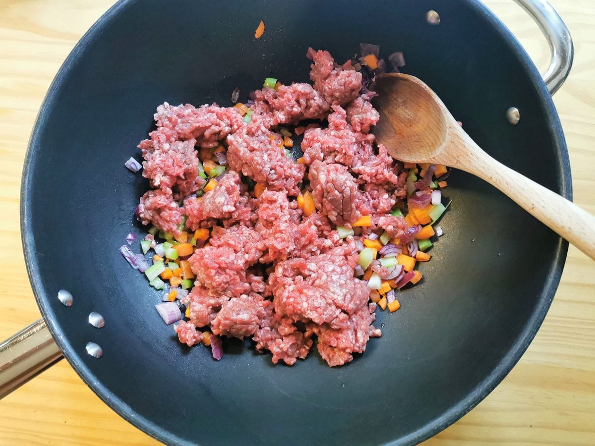 Raw ground beef added to skillet with carrots, onion and celery.