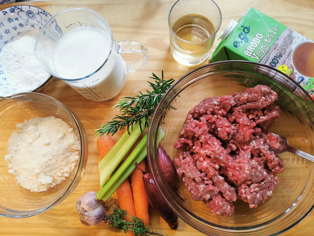 Ingredients for beef cannelloni filling and béchamel sauce on wood worktop.