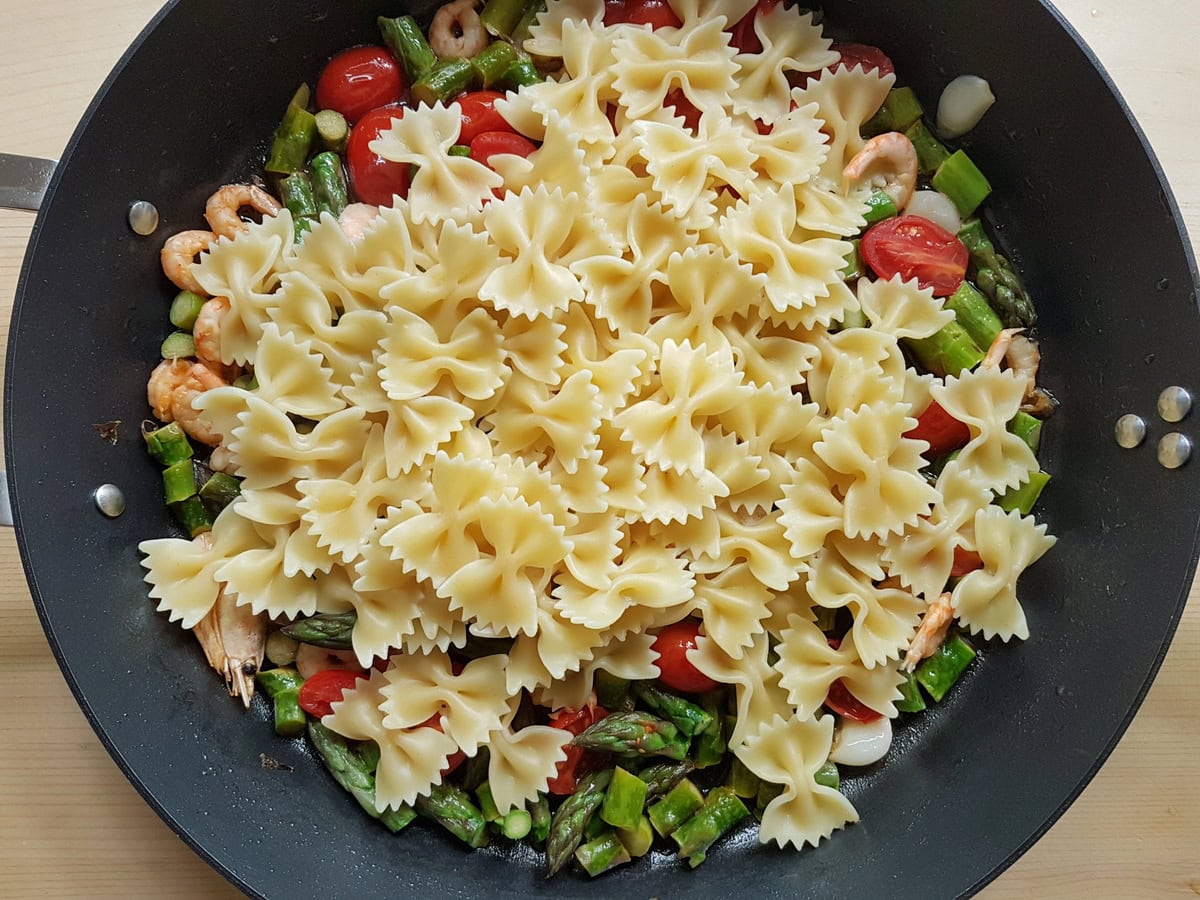 Cooked farfalle pasta added to shrimp and asparagu in skillet.