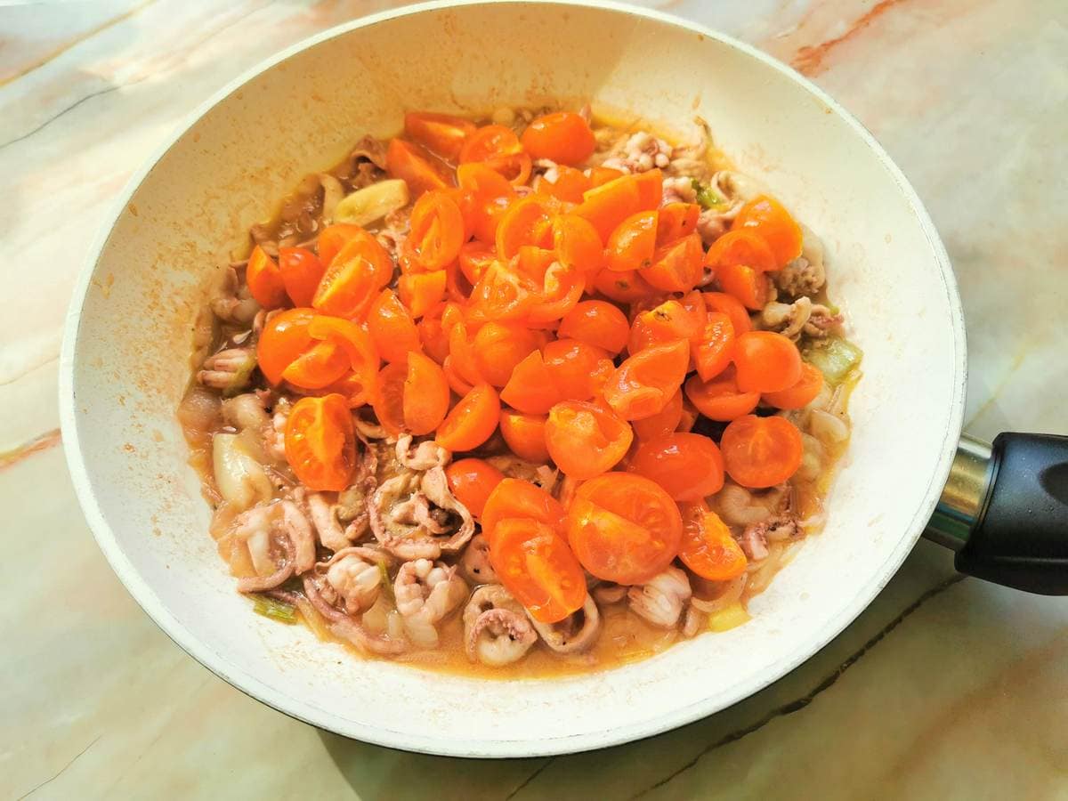 quartered cherry tomatoes in pan with squid, spring onions and garlic