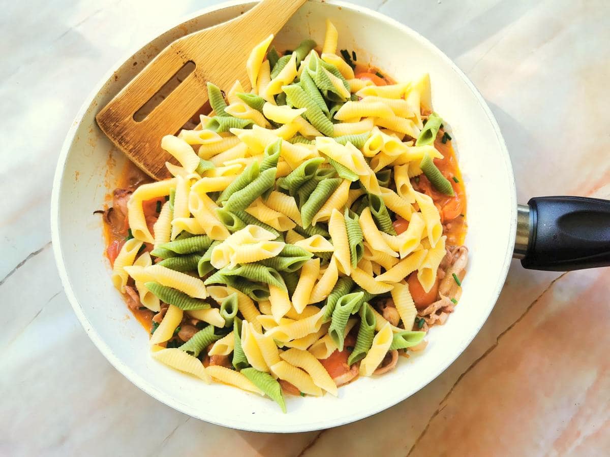 cooked green and yellow garganelli added to easy squid pasta sauce in pan