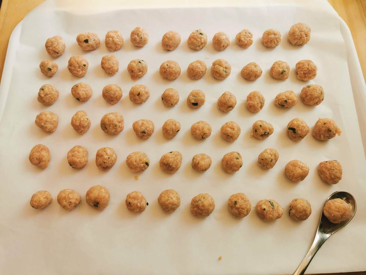 Ready uncooked hazelnut size veal meatballs on parchment papaer covered tray.