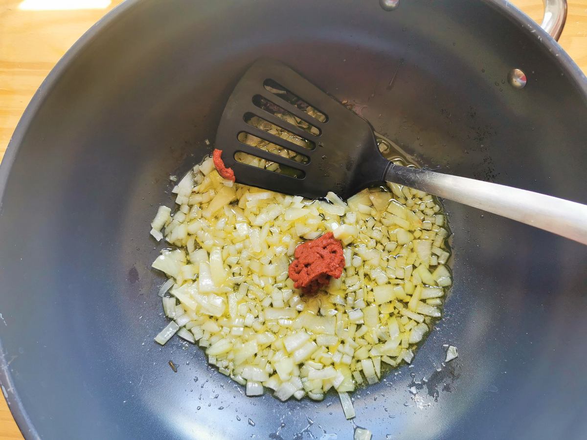 Peeled and chopped onion and a tablespoon of tomato concentrate cooking in olive oil in deep frying pan.