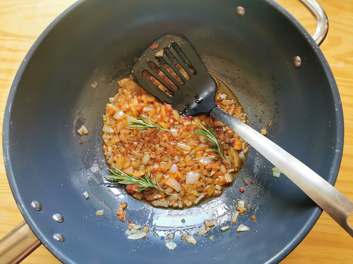 Cooked onion and tomato paste with rosemary sprigs on top in deep frying pan. 