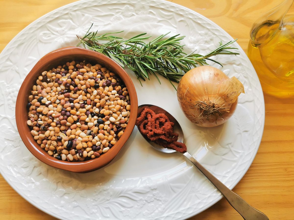 Trasimeno beans, with an onion, a sprig of rosemary and a tablespoon of tomato paste on white plate.