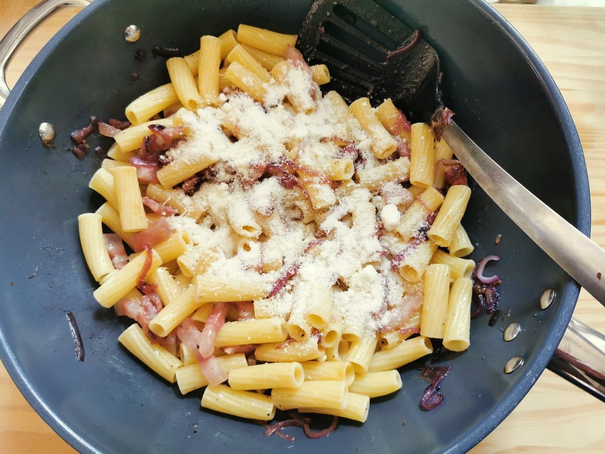 Grated pecorino added to rigatoni, red onions and guanciale in skillet.