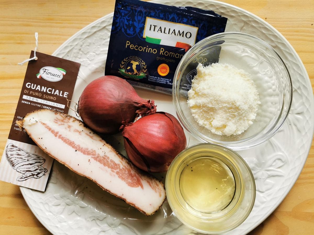Ingredients for red onion pasta with guanciale on white plate.