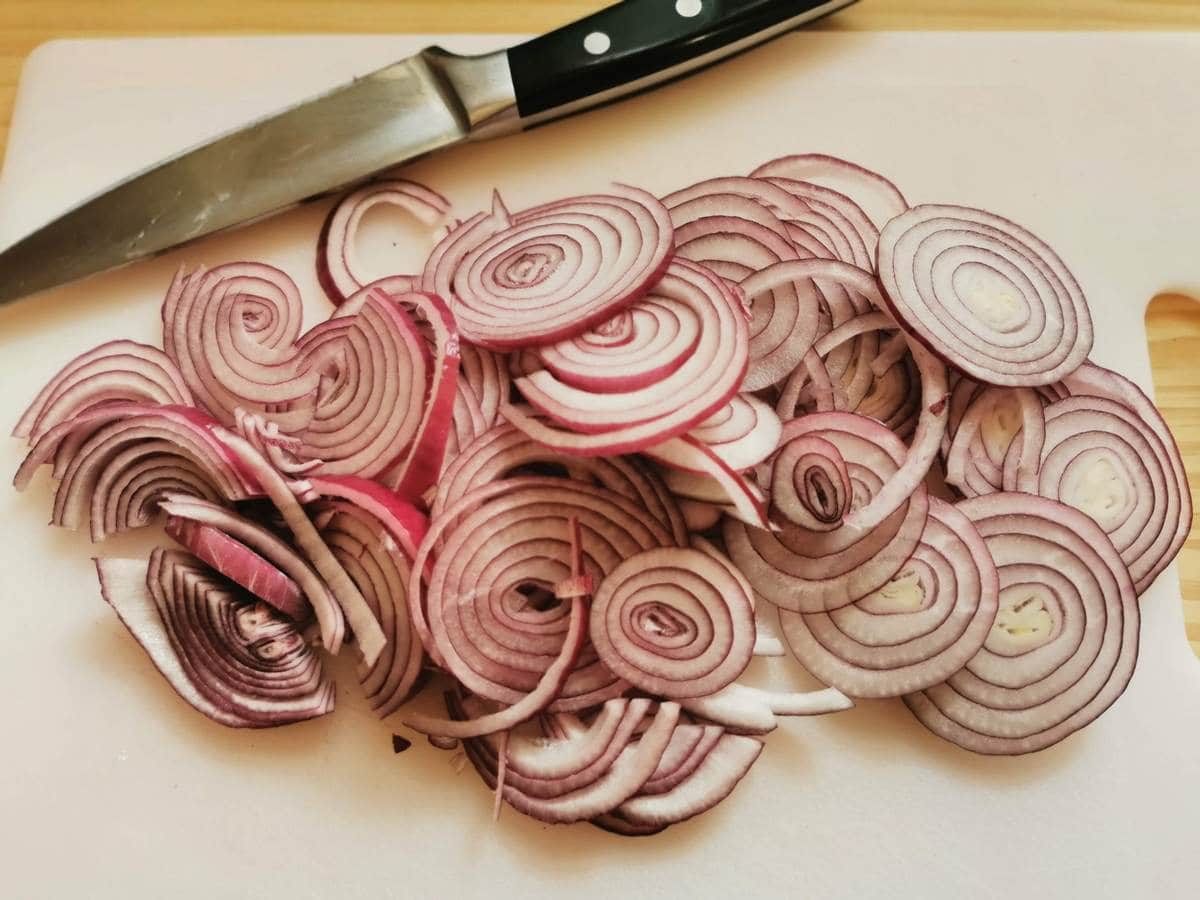 Peeled and thinly sliced red onions on white chopping board.
